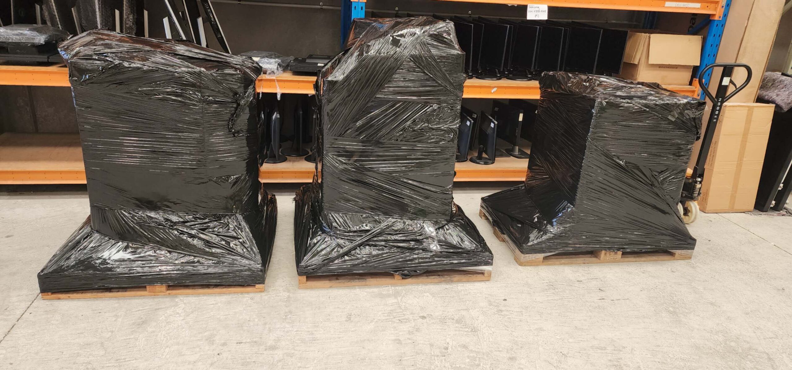 Three wrapped pallets of IT equipment in front of warehouse shelving